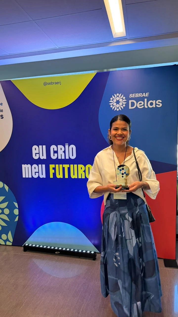 Luize Freire no palco do prêmio Sebrae Delas, segurando o troféu, ao lado da arte que diz eu crio meu futuro